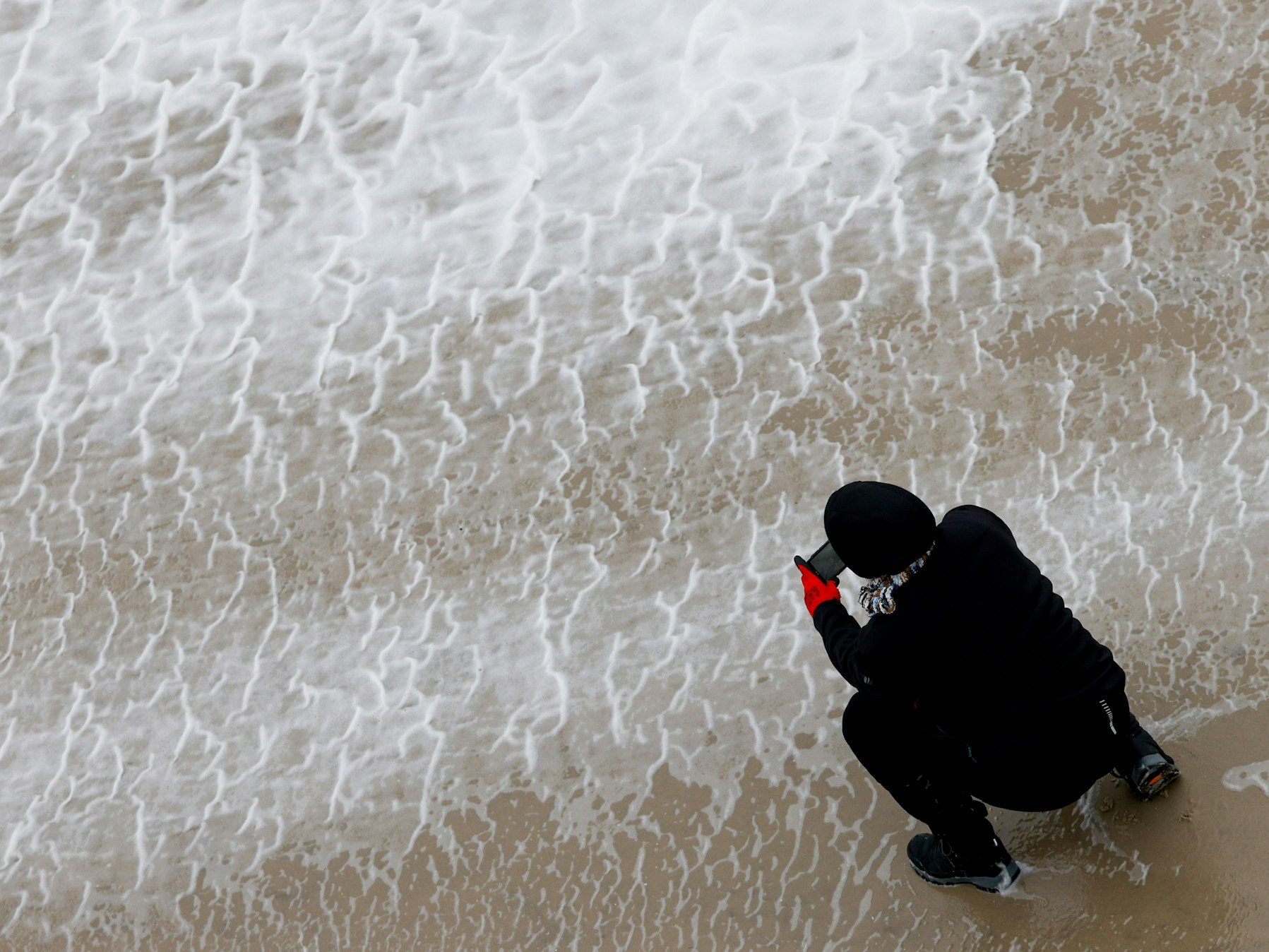 Eine Frau fotografiert mit ihrem Smartphone das von Orkanböen aufgepeitschte Wasser der Nordsee.
