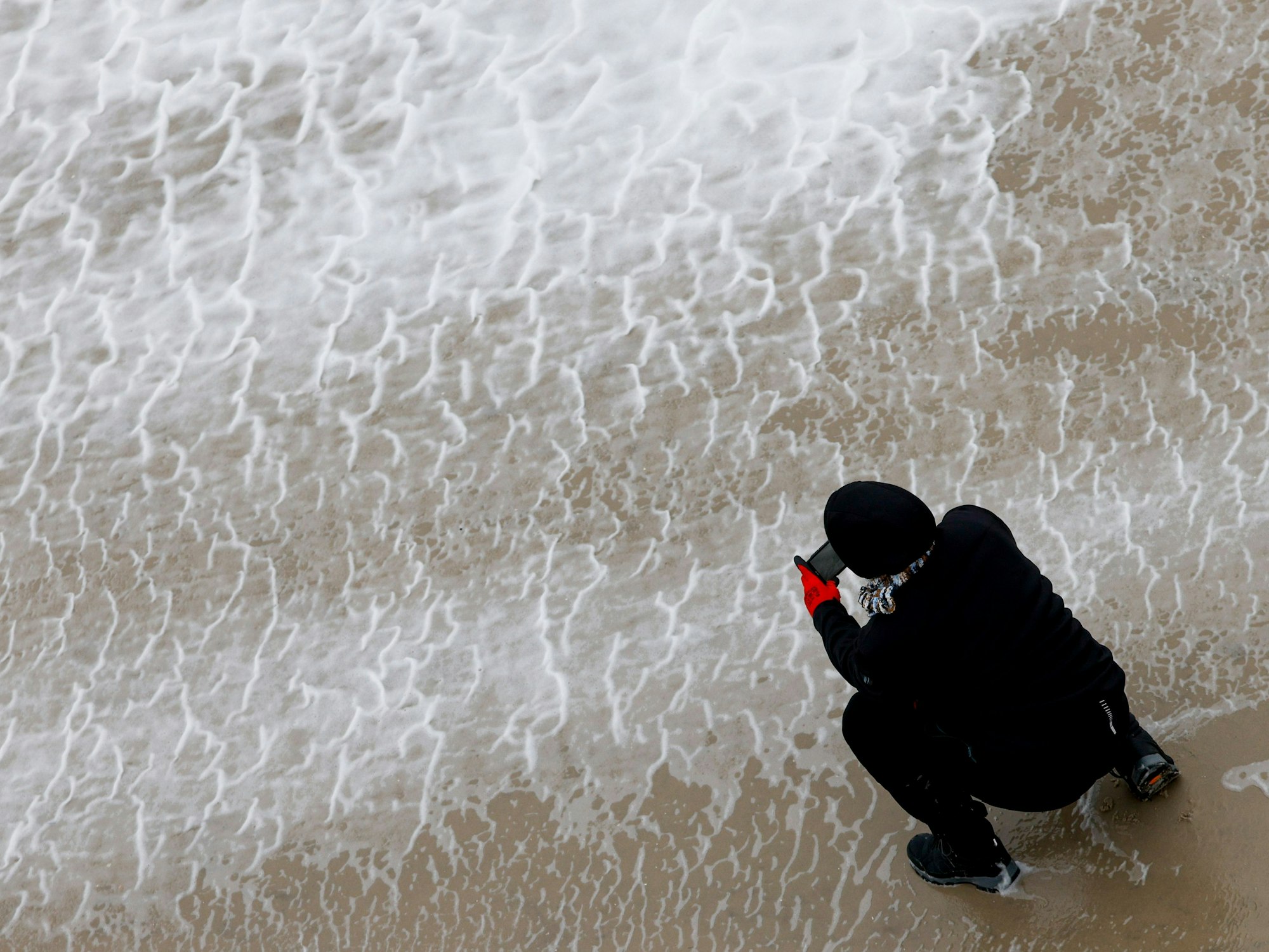Eine Frau fotografiert mit ihrem Smartphone das von Orkanböen aufgepeitschte Wasser der Nordsee.