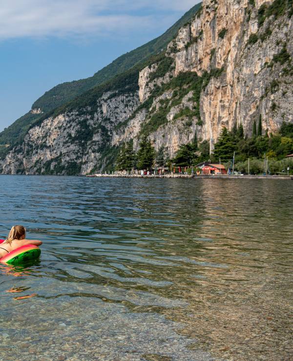 Eine Frau schwimmt auf einer Luftmatratze im klaren Wasser des Gardasees.