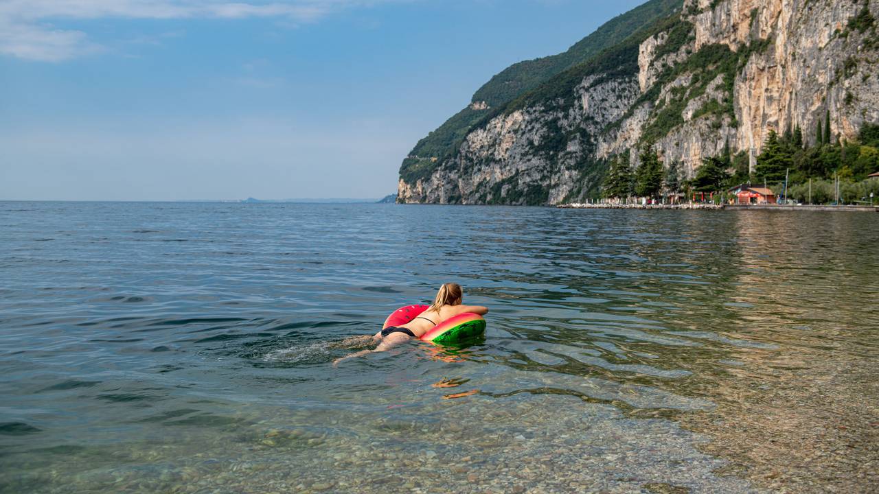 Eine Frau schwimmt auf einer Luftmatratze im klaren Wasser des Gardasees.