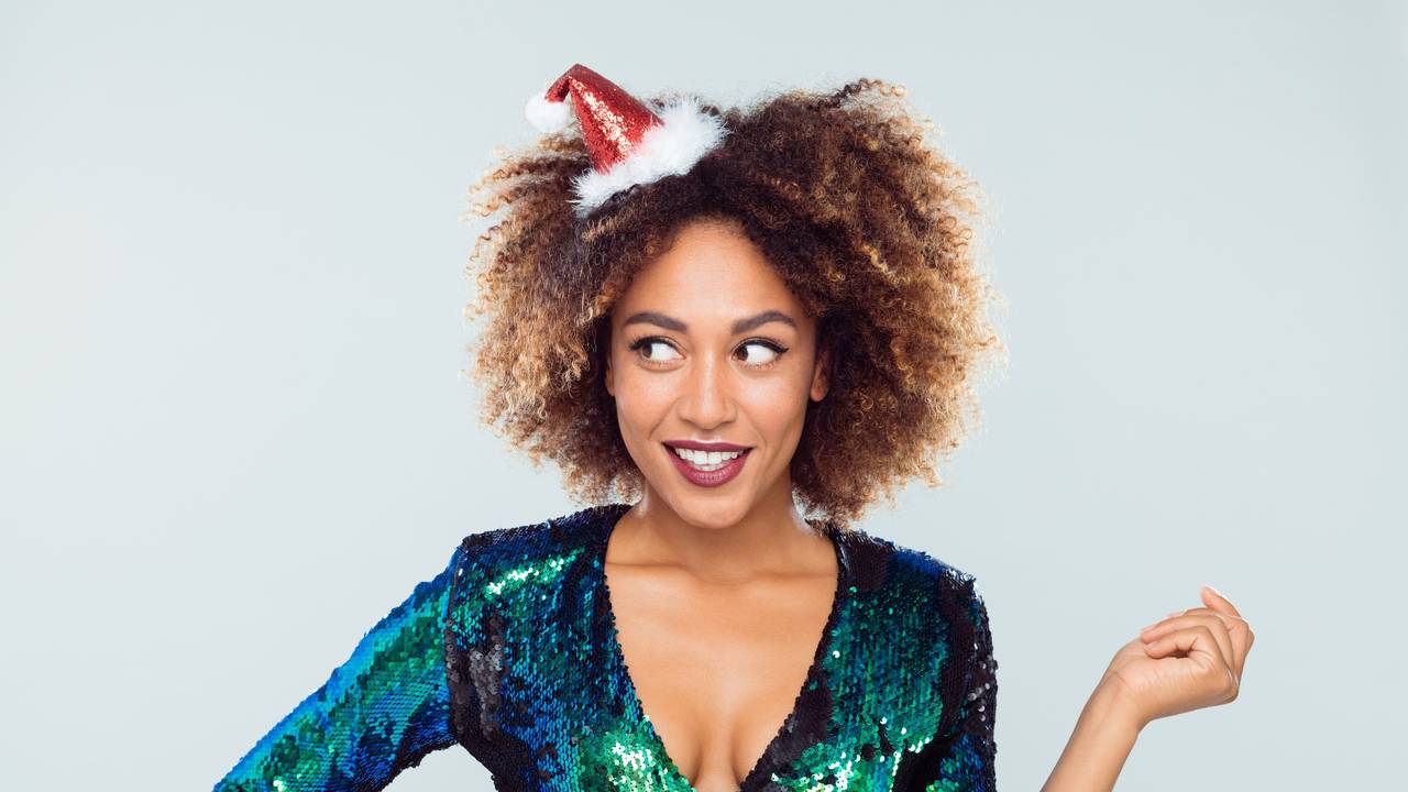 Fröhliche junge Frau im Glitzerkleid mit Weihnachtshütchen