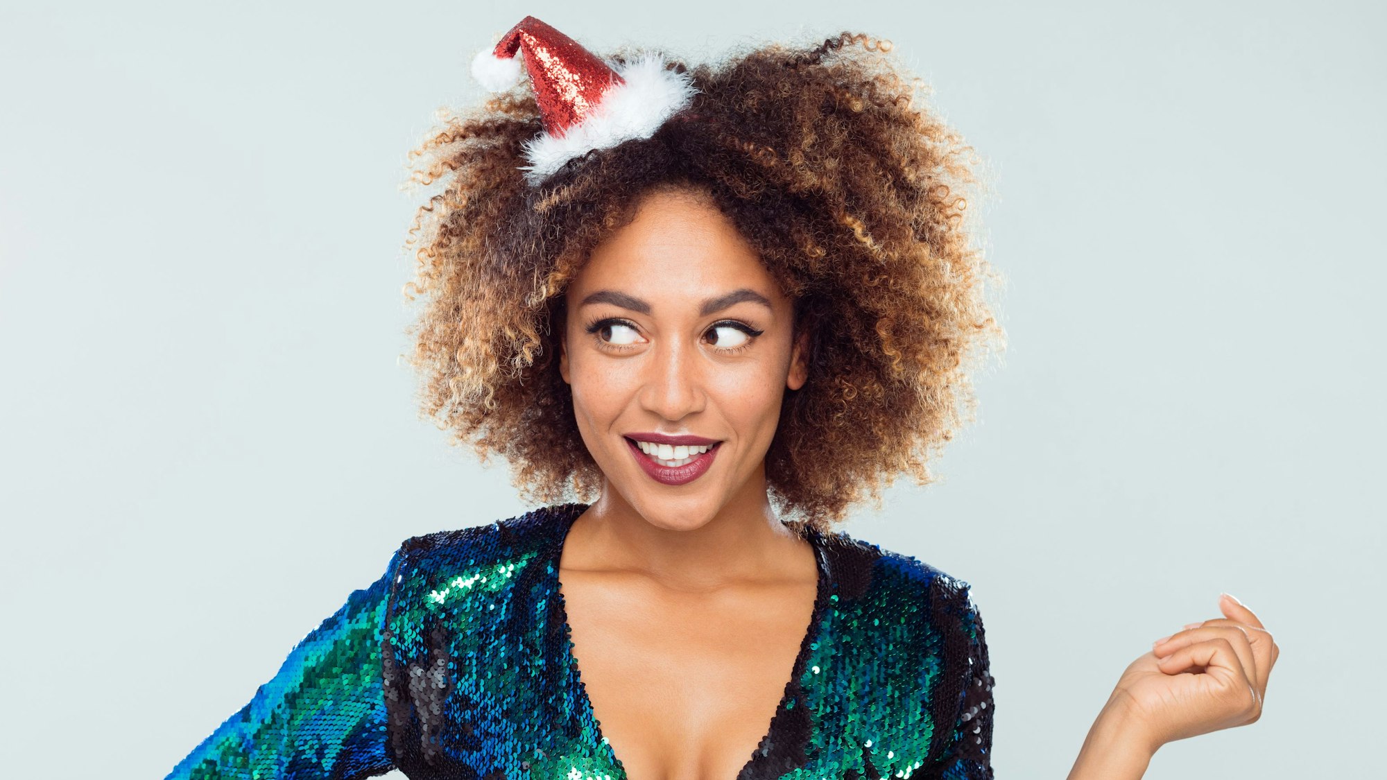 Fröhliche junge Frau im Glitzerkleid mit Weihnachtshütchen