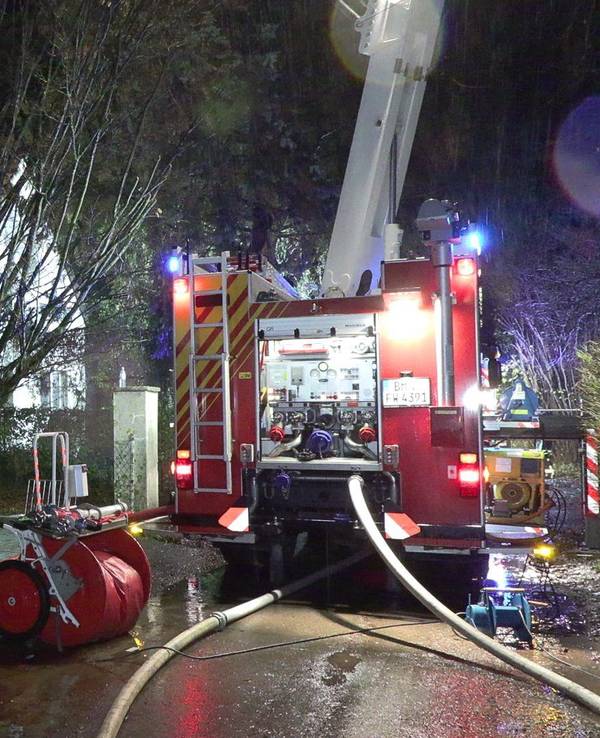 Feuerwehrleute stehen mit ihrem Fahrzeug vor einem Haus.