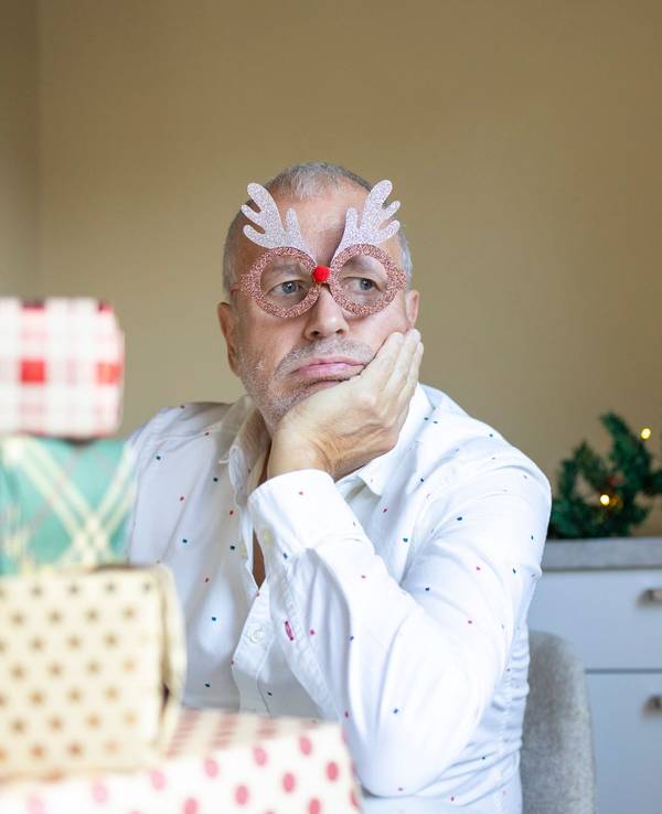 Upset aged man with grey hairs sitting near Christmas presents