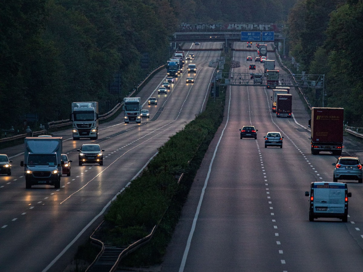 Autos und Lkw sind auf der A3 in Richtung Köln unterwegs, im Hintergrund ist die Sonne zu sehen.