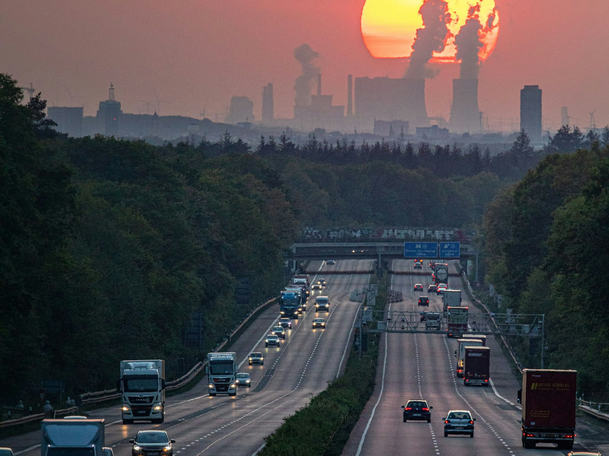 Autos und Lkw sind auf der A3 in Richtung Köln unterwegs, im Hintergrund ist die Sonne zu sehen.