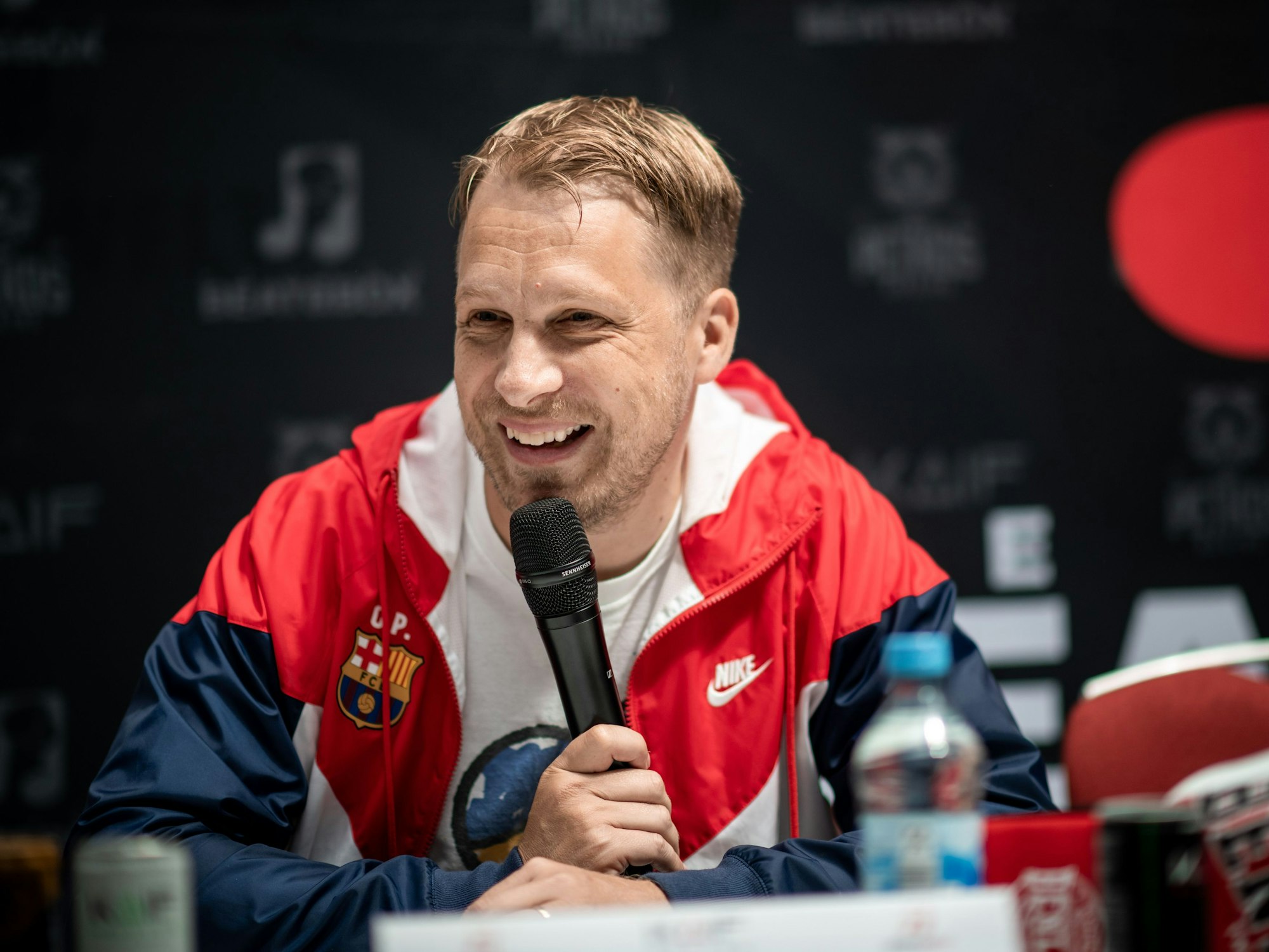 Oliver Pocher sitzt bei der Pressekonferenz im Westfield Centro in Oberhausen auf einer Bühne und lacht.