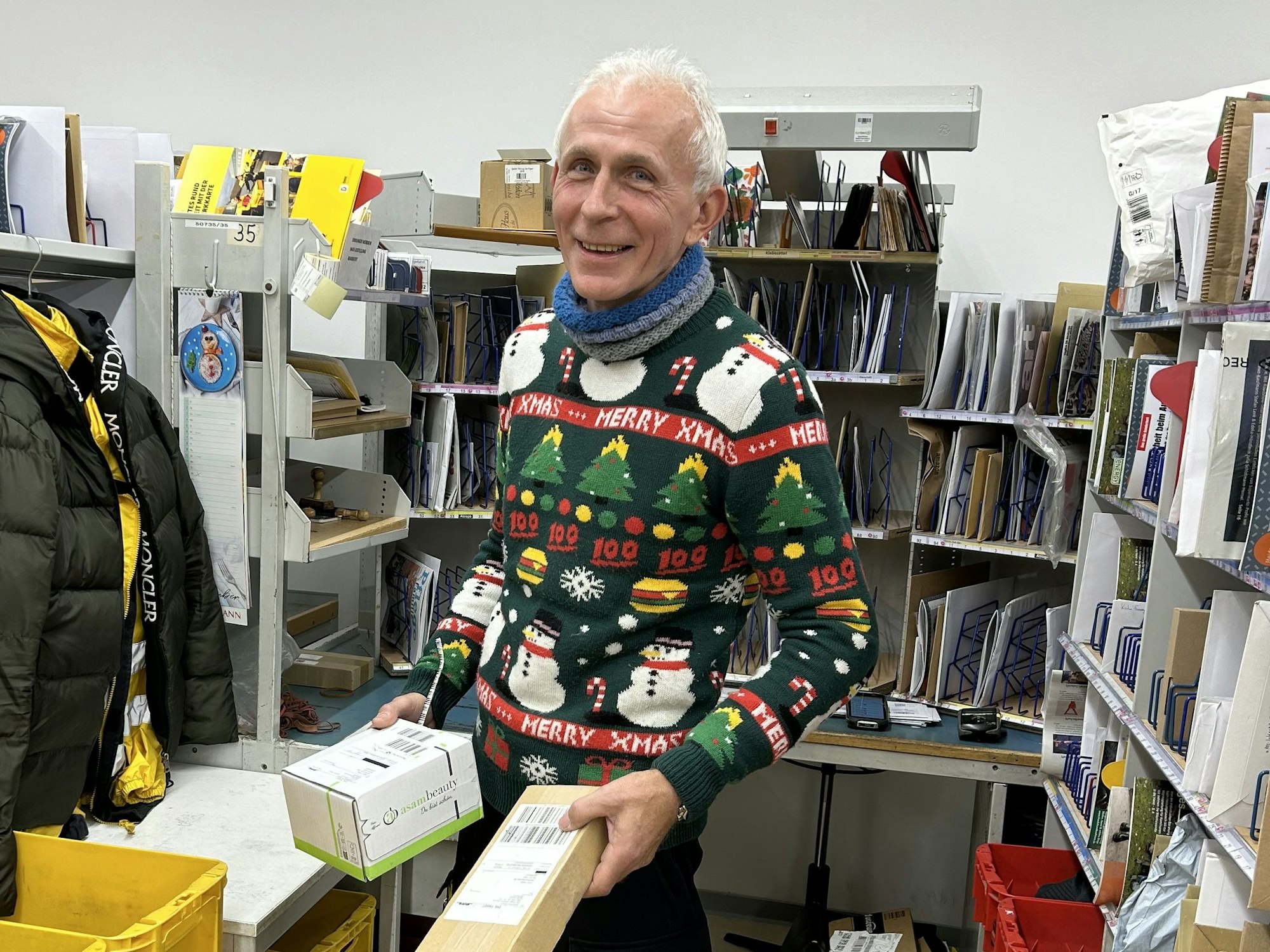 Zusteller Eugen Mularczyk steht mit Paketen in der Hand in einem Lager.