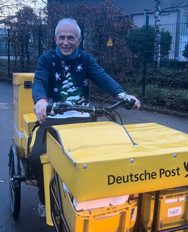 Ein Mann mit grauen Haaren liefert für die Deutsche Post auf einem Fahrrad Post aus.