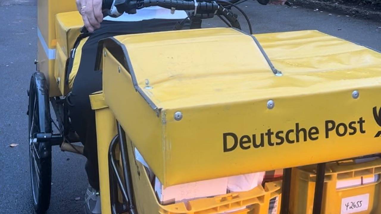 Ein Mann mit grauen Haaren liefert für die Deutsche Post auf einem Fahrrad Post aus.