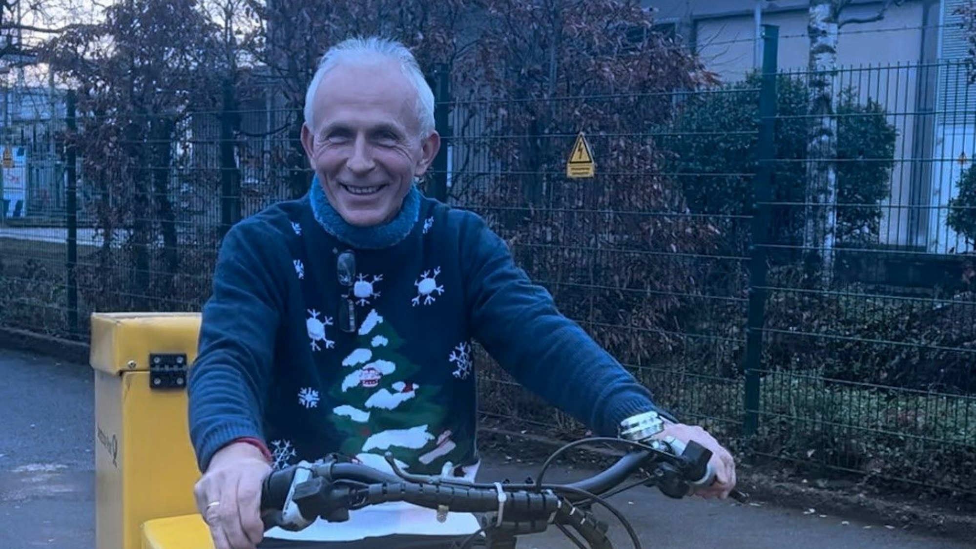 Ein Mann mit grauen Haaren liefert für die Deutsche Post auf einem Fahrrad Post aus.