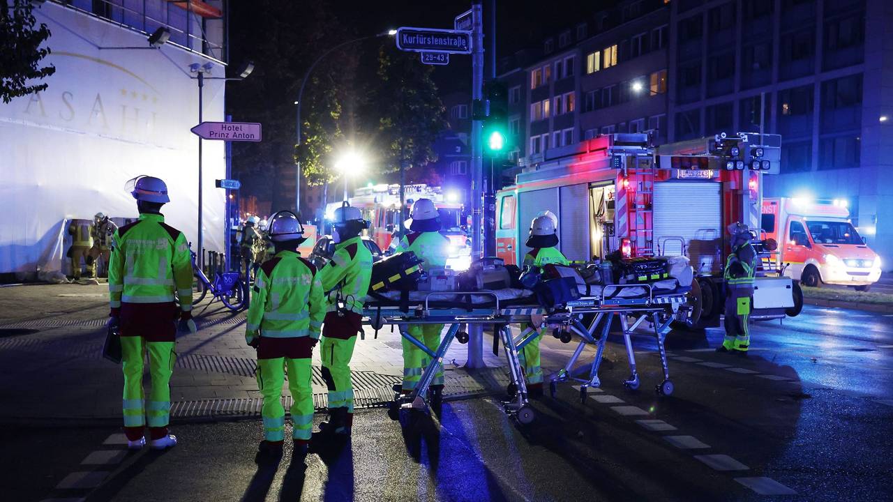 Mehrere Einsatzkräfte der Feuerwehr stehen vor einem Gebäude, an der Straße parkt ein Löschfahrzeug.