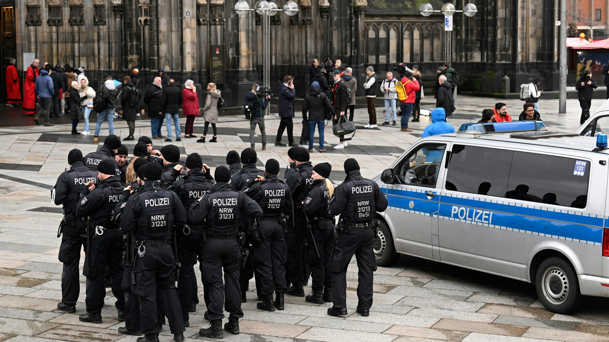 Einige Einsatzkräfte der Polizei stehen ganz in schwarz gekleidet vor dem Haupteingang des Kölner Doms.