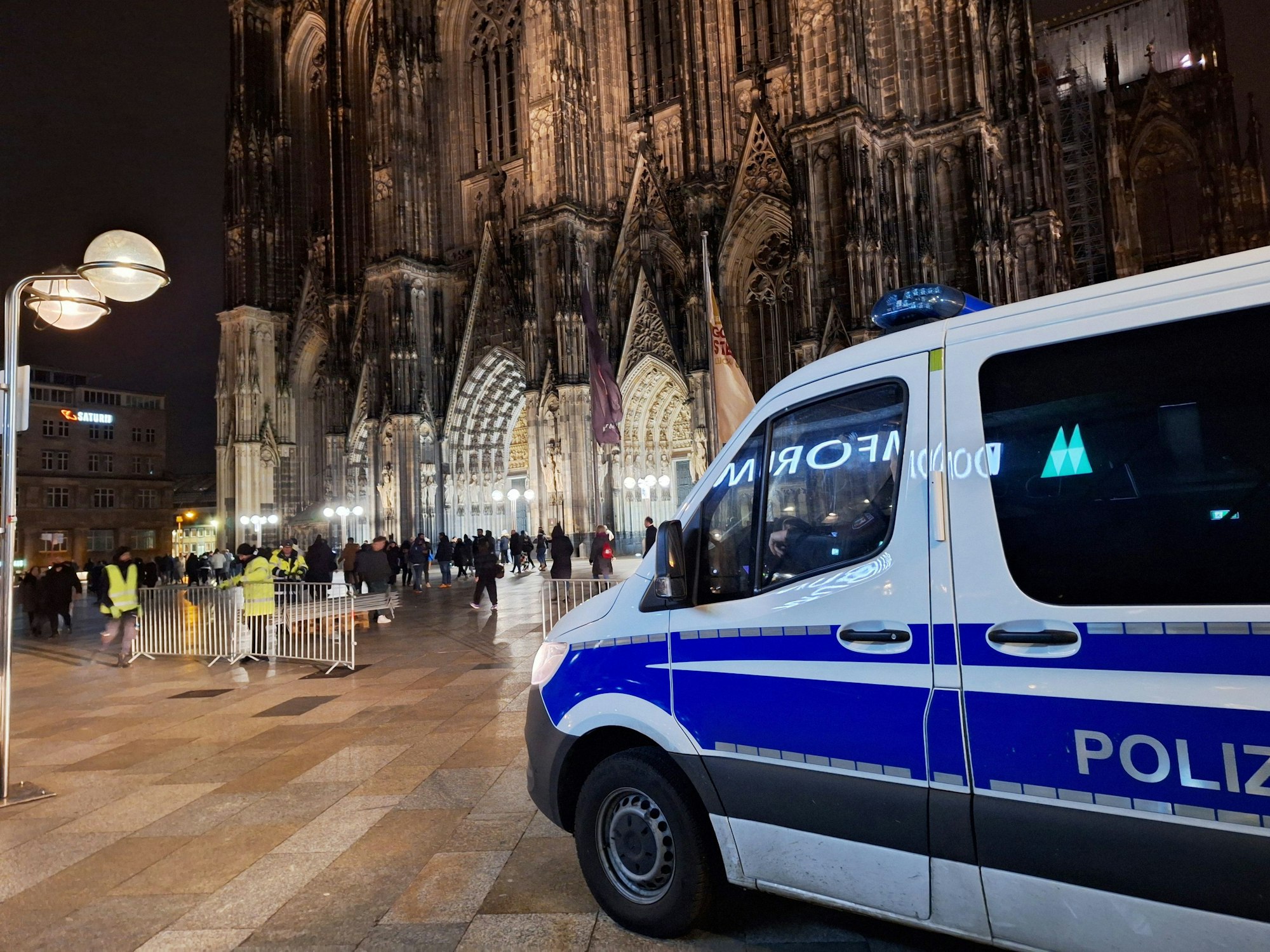 Ein Polizei-Auto steht auf der Freifläche vor dem Kölner Dom, im Hintergrund sind viele Menschen zu sehen.