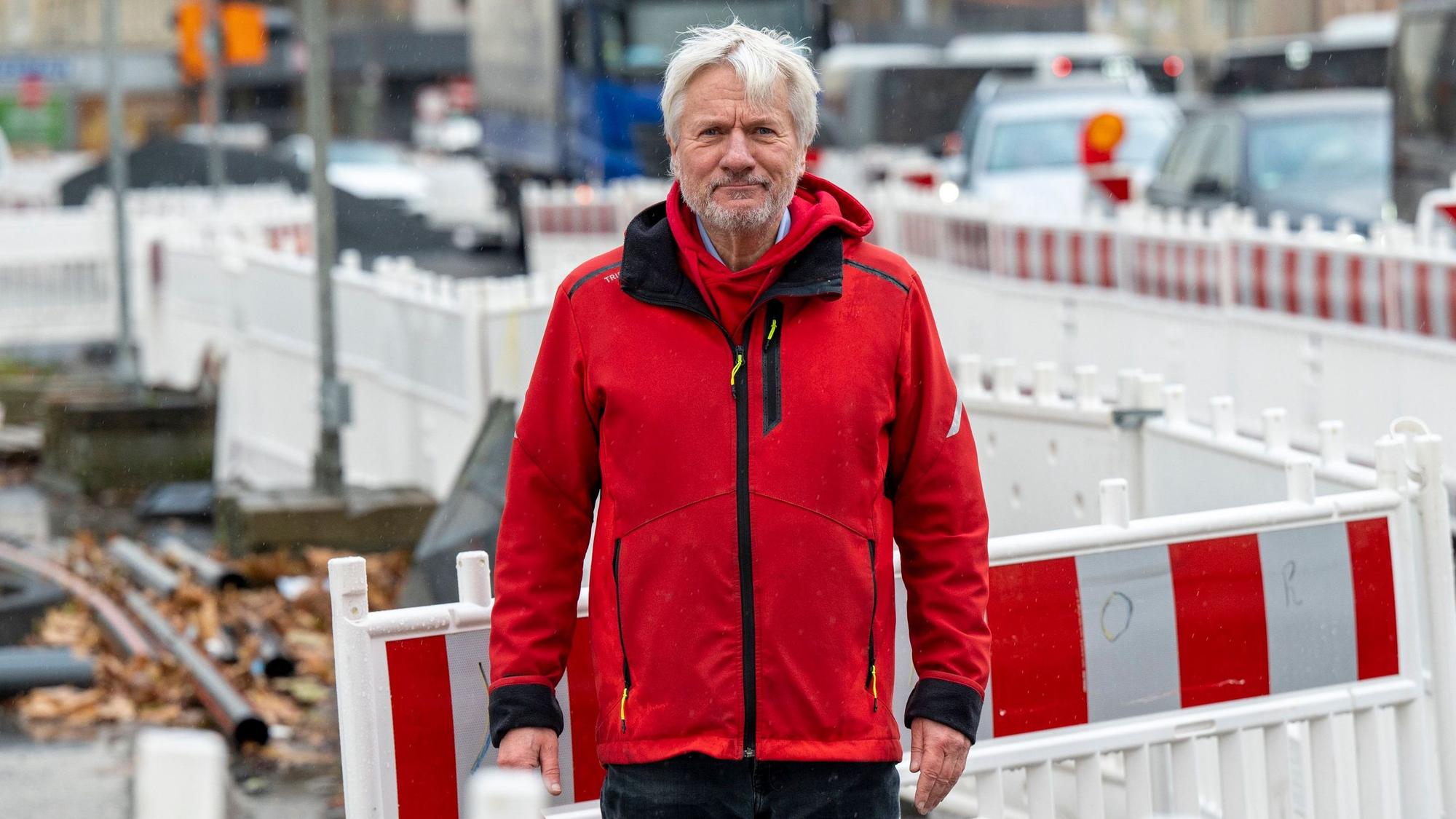 Jürgen Becker steht zwischen Baustellenbaken auf einer Baustelle in Köln.