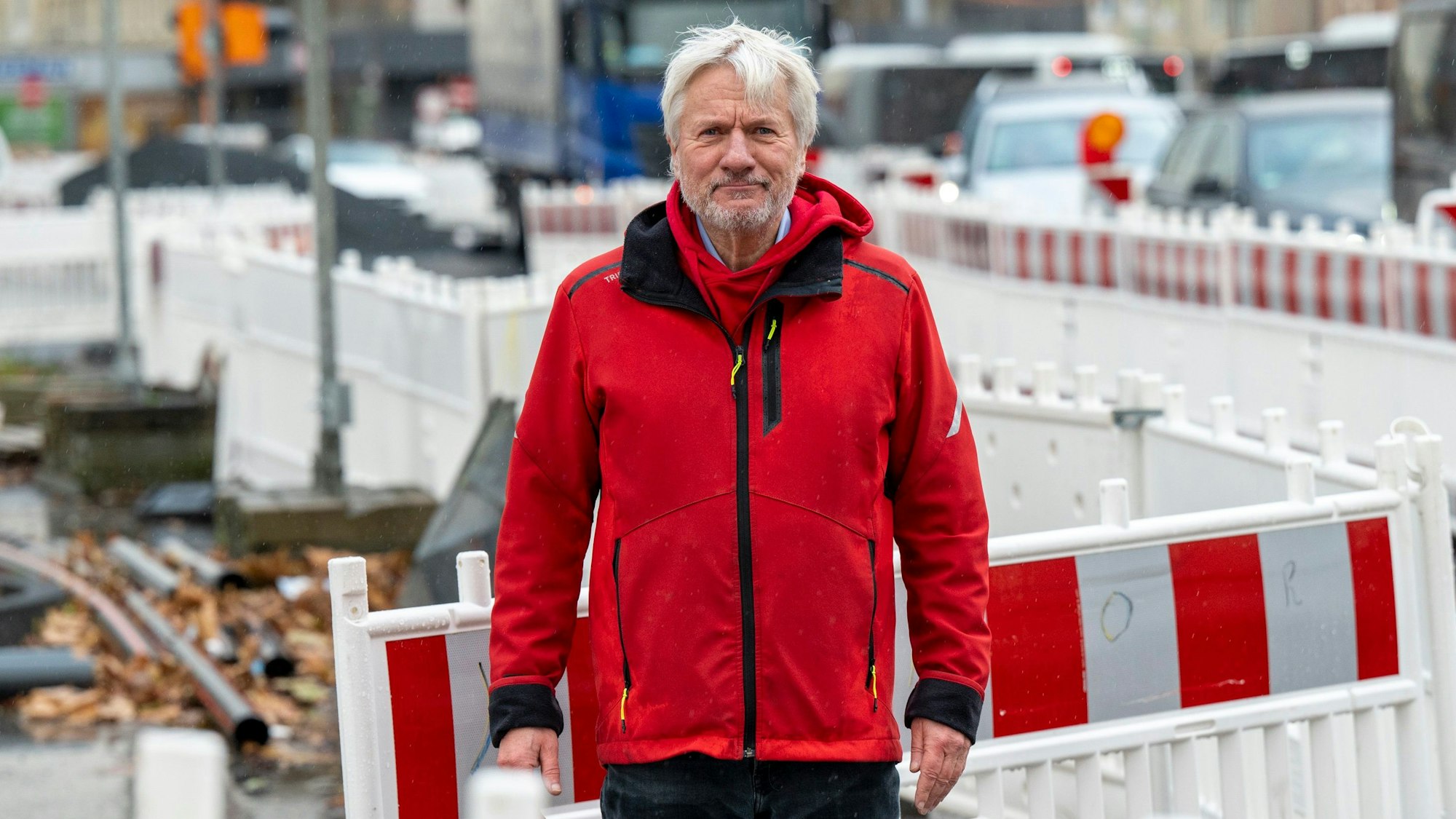 Jürgen Becker steht zwischen Baustellenbaken auf einer Baustelle in Köln.