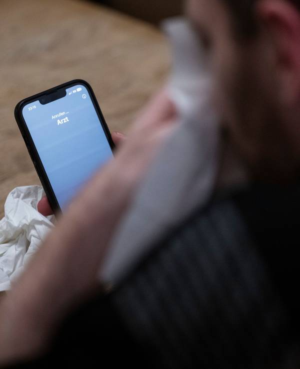 Ein Mann hält ein Taschentuch in einer Hand und ein Telefon mit dem Schriftzug „Arzt“ in der Anderen.