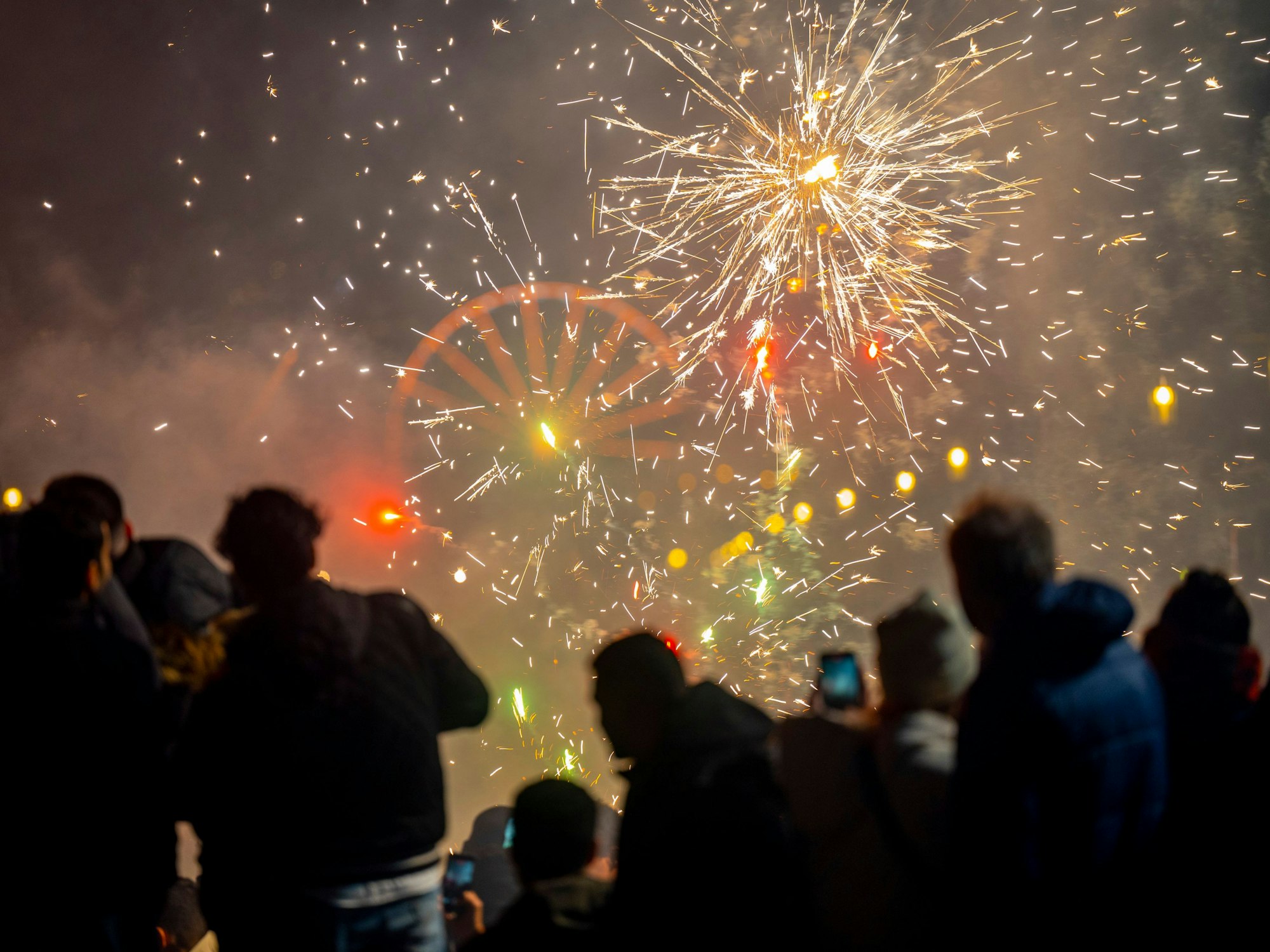 Menschen schauen in den Nachthimmel, an dem Feuerwerksraketen explodieren.