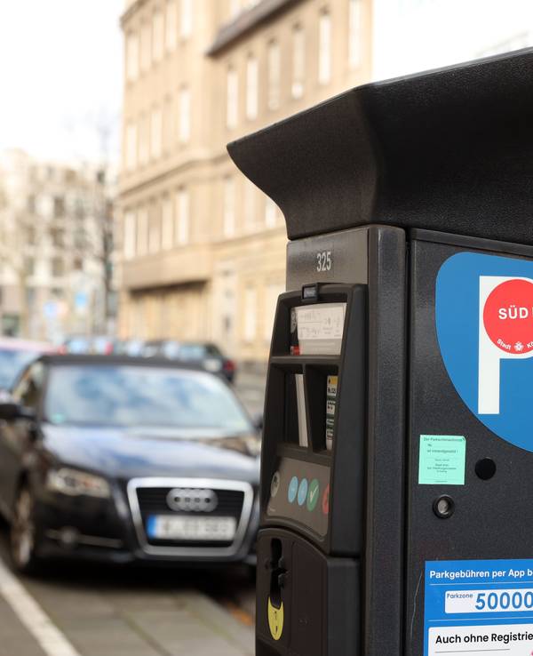 Ein Parkscheinautomat in einer Kölner Straße, im Hintergrund sind Autos zu sehen.