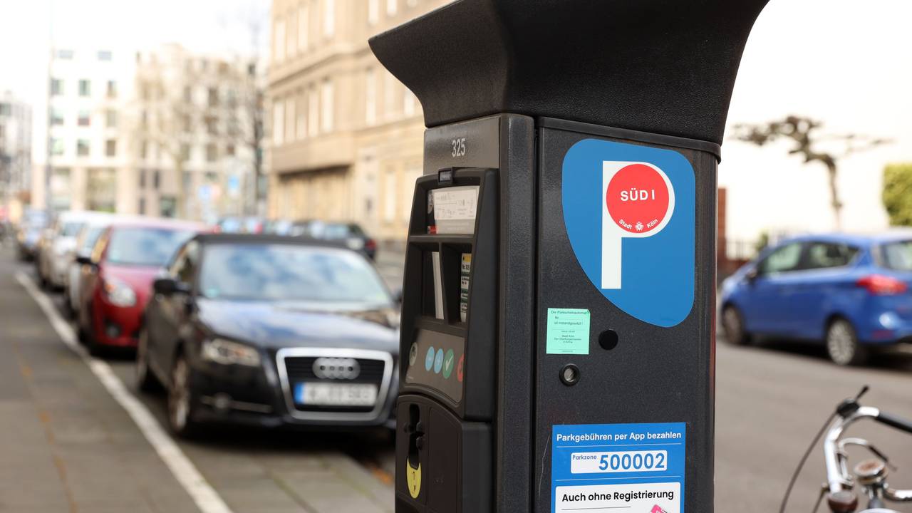 Ein Parkscheinautomat in einer Kölner Straße, im Hintergrund sind Autos zu sehen.