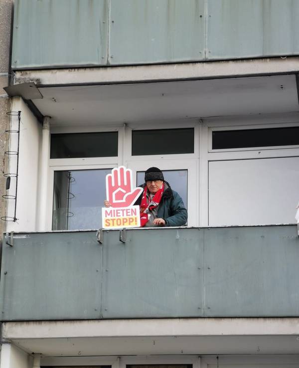Rainer Kippe steht auf einem Balkon und hält ein Plakat mit der Forderung "Mieten Stopp" in der Hand.