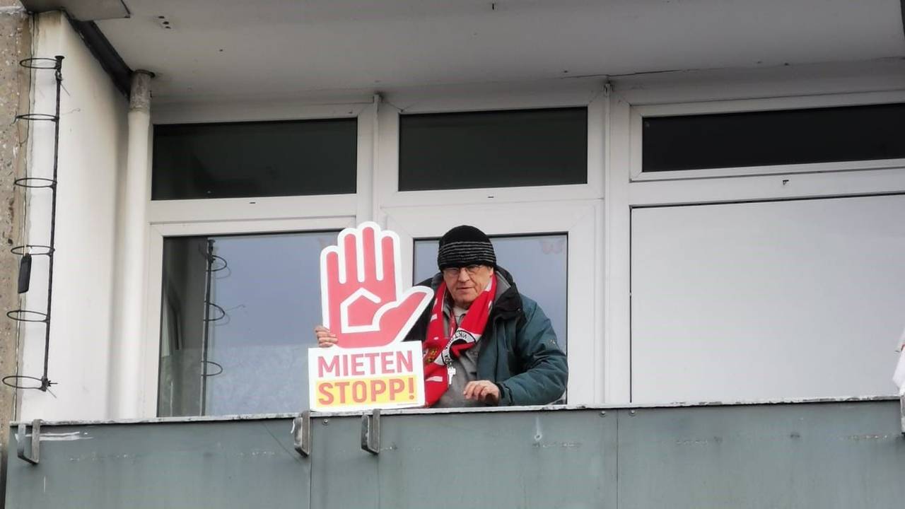 Rainer Kippe steht auf einem Balkon und hält ein Plakat mit der Forderung "Mieten Stopp" in der Hand.