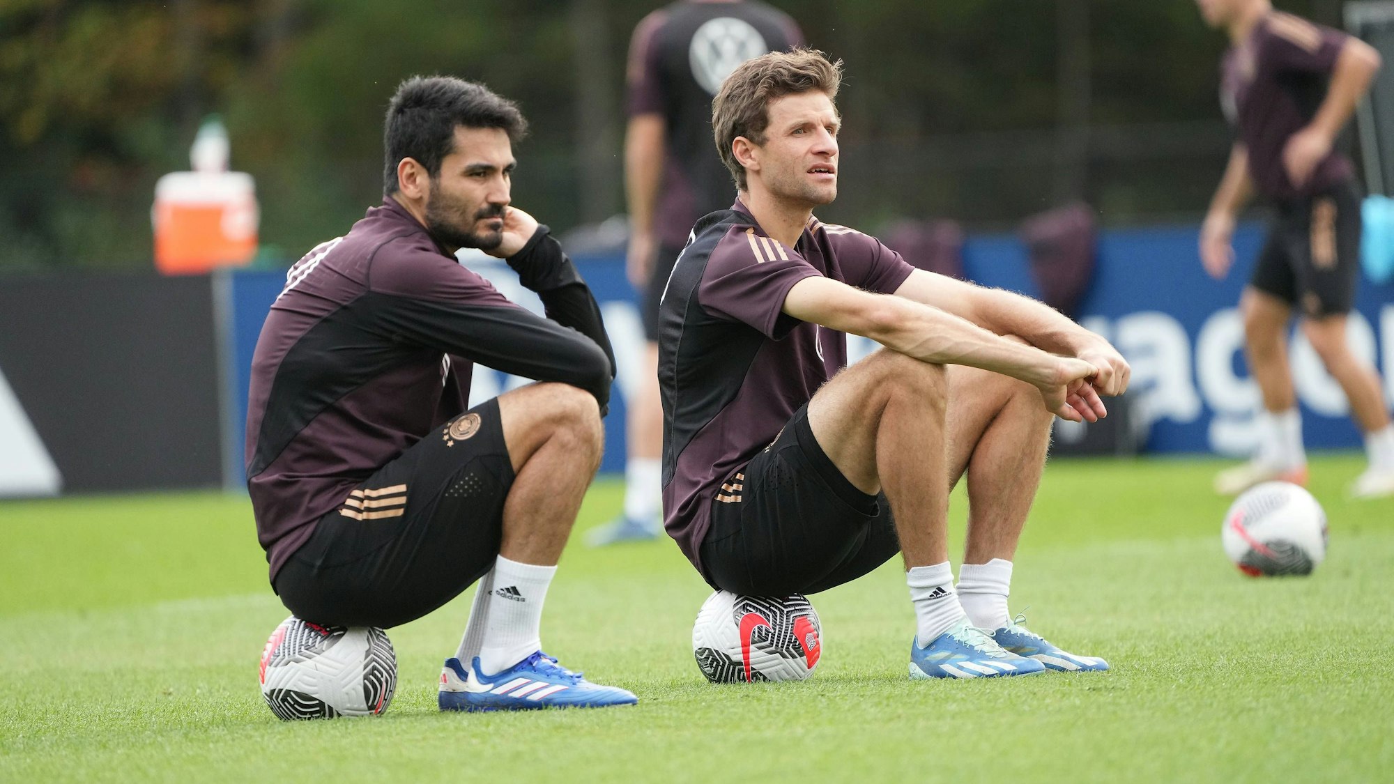 Ilkay Gündogan und Thomas Müller sitzen im Training der deutschen Nationalmannschaft auf Bällen und unterhalten sich.