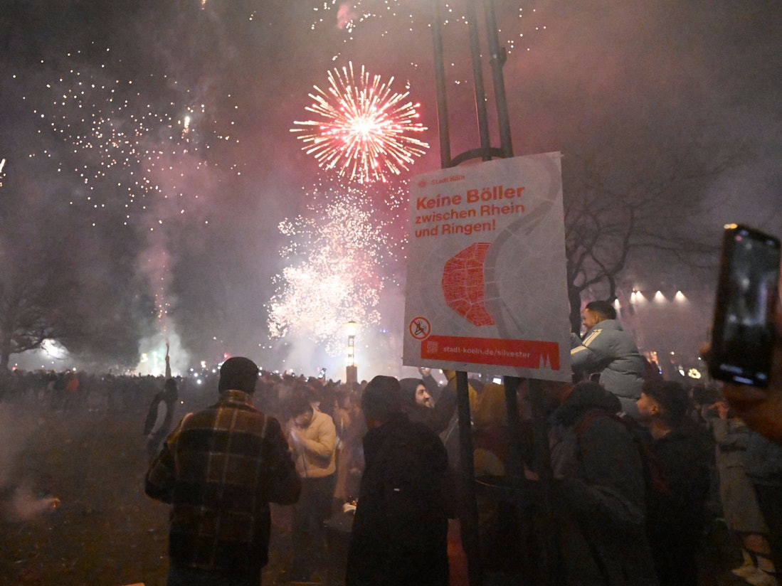 Menschen zünden in der Altstadt Feuerwerkskörper vor dem Böllerverbotsplakat.