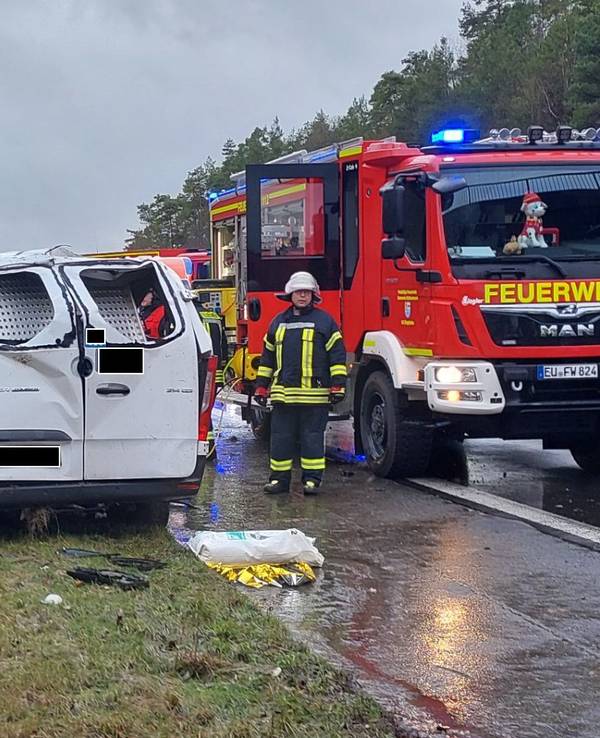 Ein schwer beschädigter Kleintransporter steht neben der A1-Fahrbahn, das Dach ist stark eingedellt. Daneben steht ein Fahrzeug der Feuerwehr.