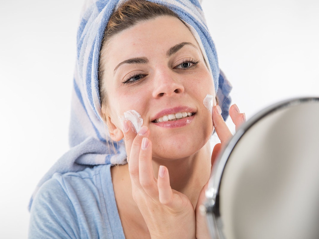 Eine Frau trägt vor einem Spiegel eine Gesichtscreme auf.