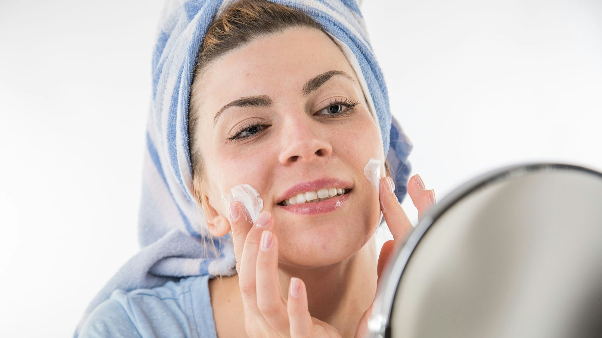 Eine Frau trägt vor einem Spiegel eine Gesichtscreme auf.