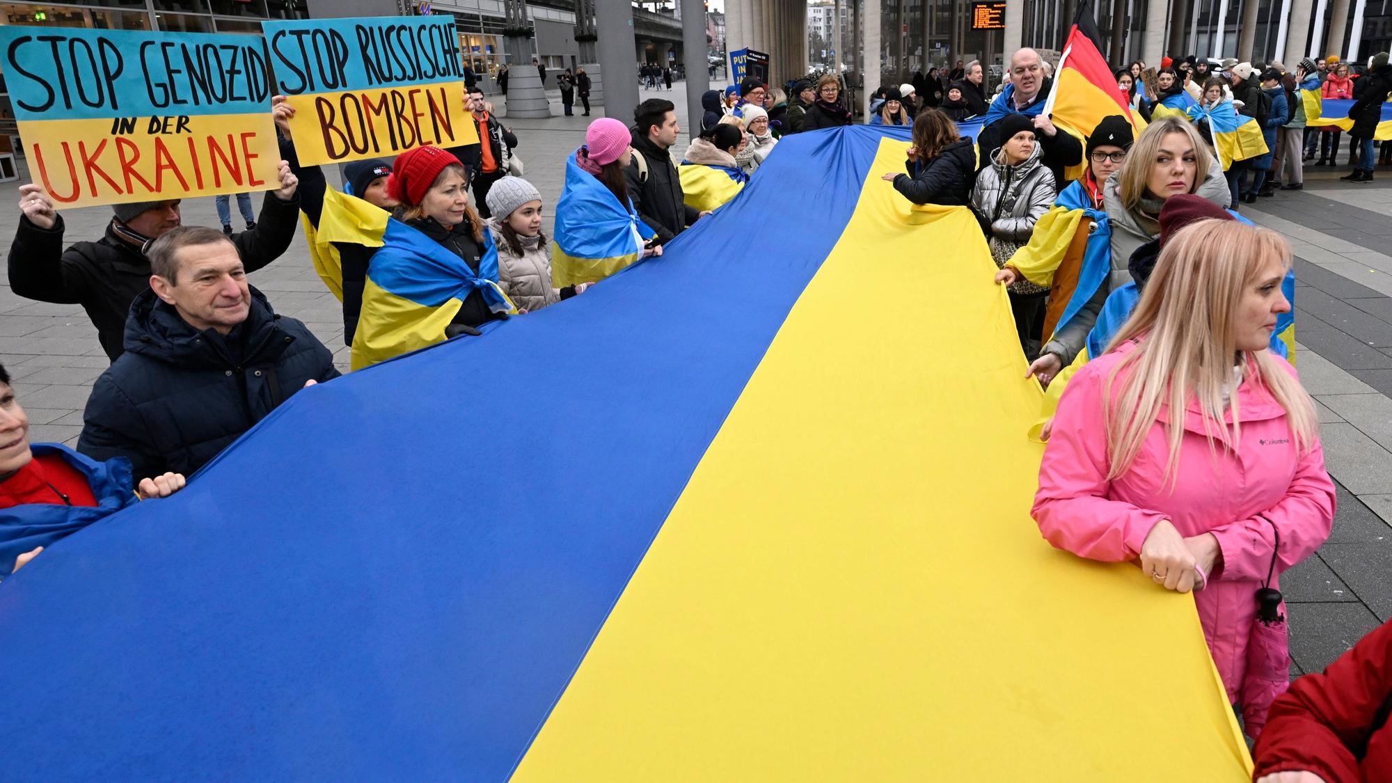 Demonstranten und Demonstrantinnen halten am Kölner Hauptbahnhof eine riesige Fahne der Ukraine in den Händen.