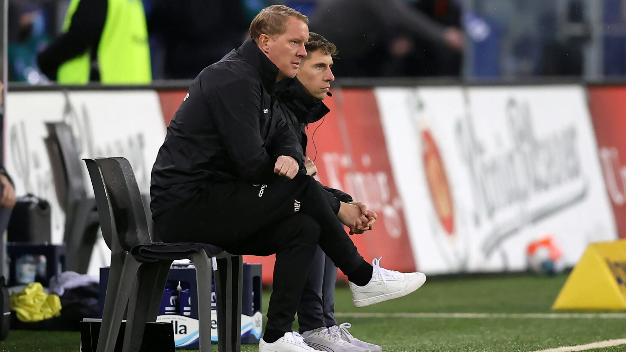 Timo Schultz und sein damaliger Co-Trainer Loic Favé sitzen beim Spiel des FC St. Paul gegen den Hamburger SV nebeneinander am Spielfeldrand.