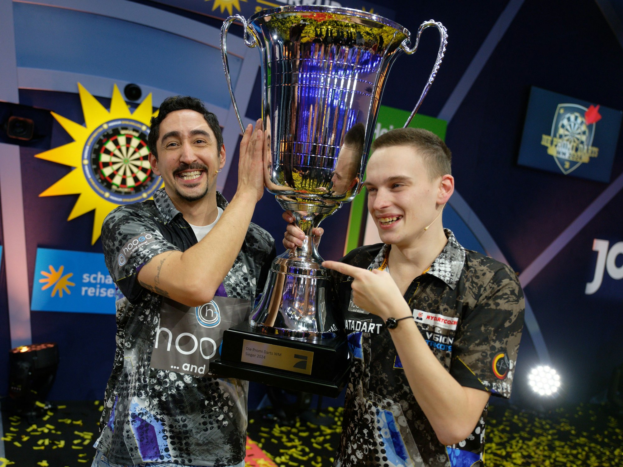 Die Gewinner der ProSieben Fernsehshow „Promi-Darts-WM 2024“: Eko Fresh (links) und Ricardo Pietreczko stehen mit ihrem Pokal auf der Bühne.