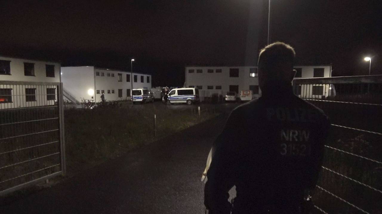 Ein Polizist steht am Tor zu einer Flüchtlingsunterkunft in Sankt Augustin. Eine vermisste Jugendliche ist am Sonntagabend tot in der Unterkunft gefunden worden.