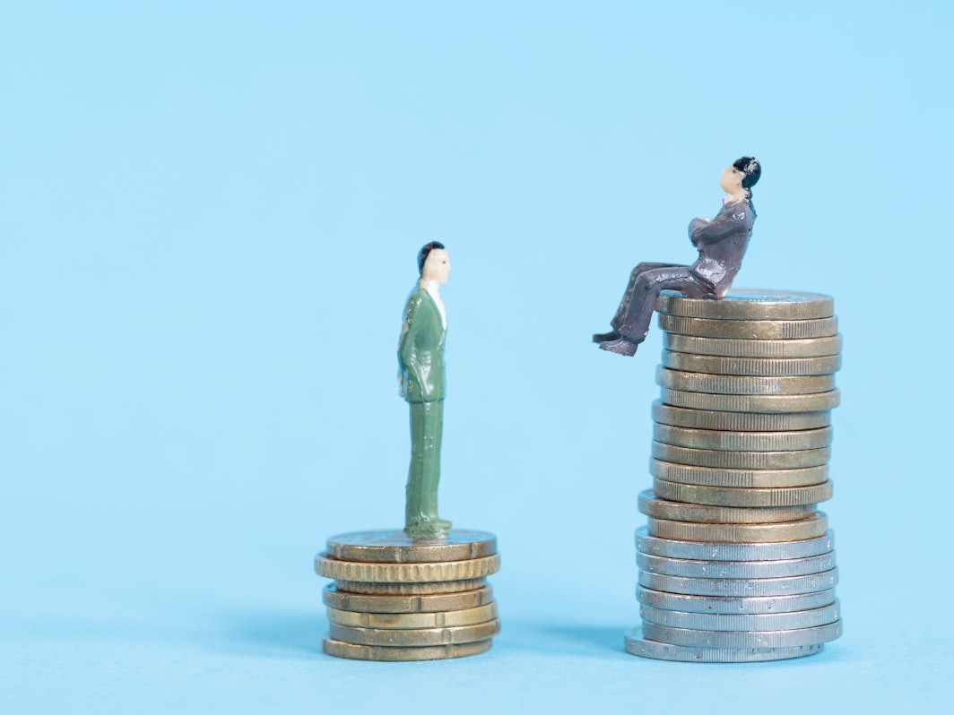 Zwei Figuren stehen auf zwei unterschiedlich hohen Stapeln aus Münzen.