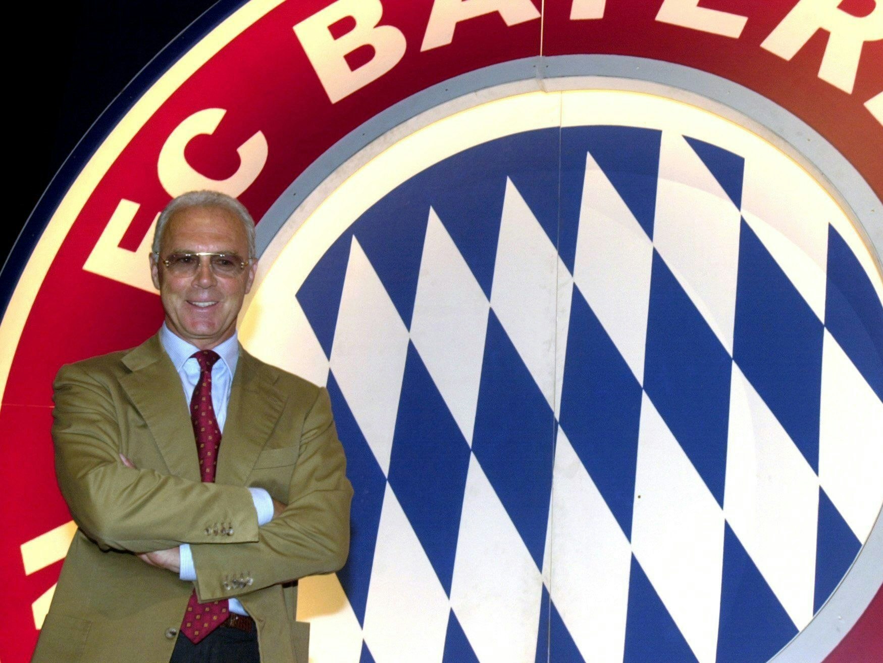 Franz Beckenbauer vor dem Logo des FC Bayern München.