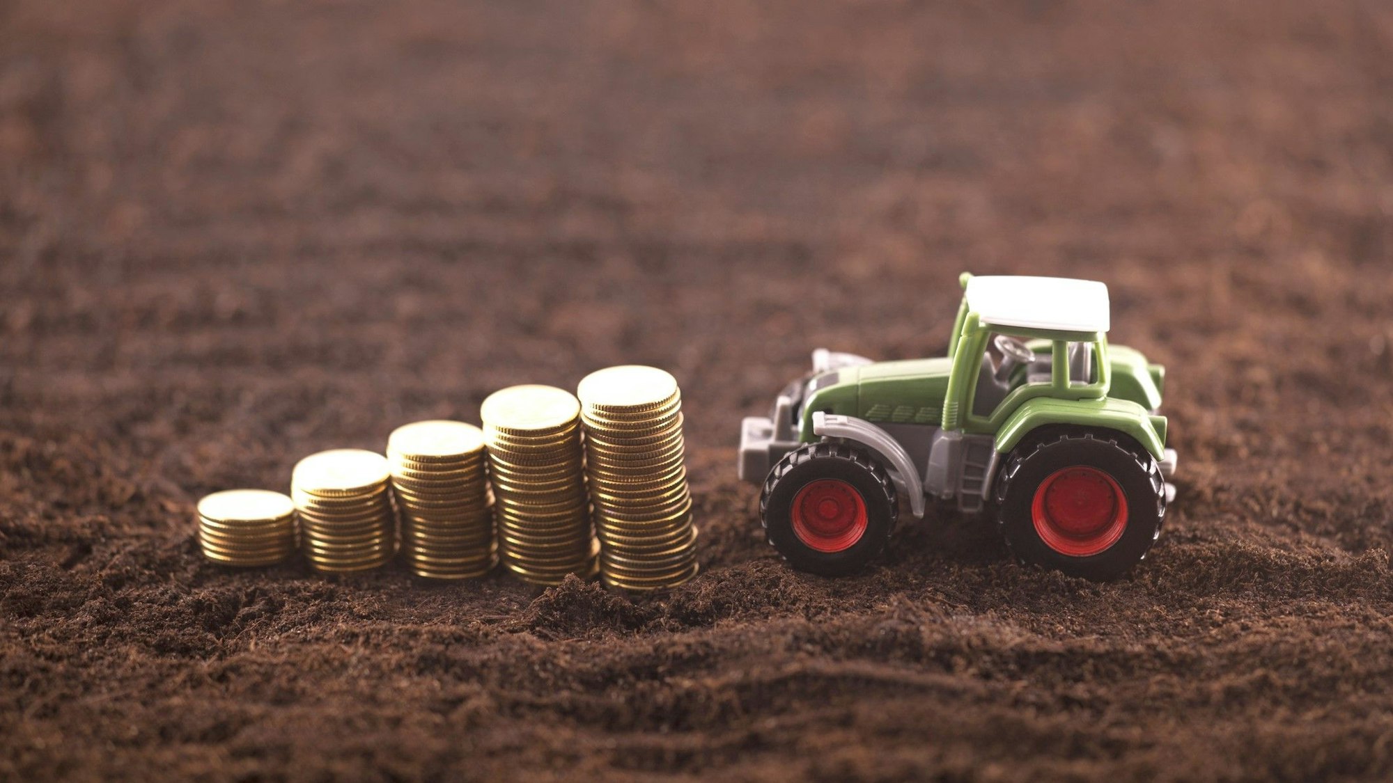 Ein Spielzeugtraktor fährt auf einen Stapel mit Münzen zu.