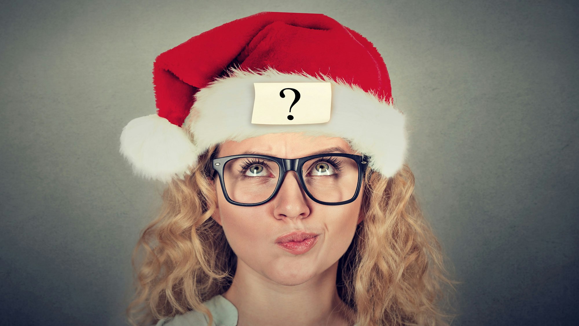 Eine junge Frau mit Santa Claus-Mütze und fragendem Gesichtsausdruck