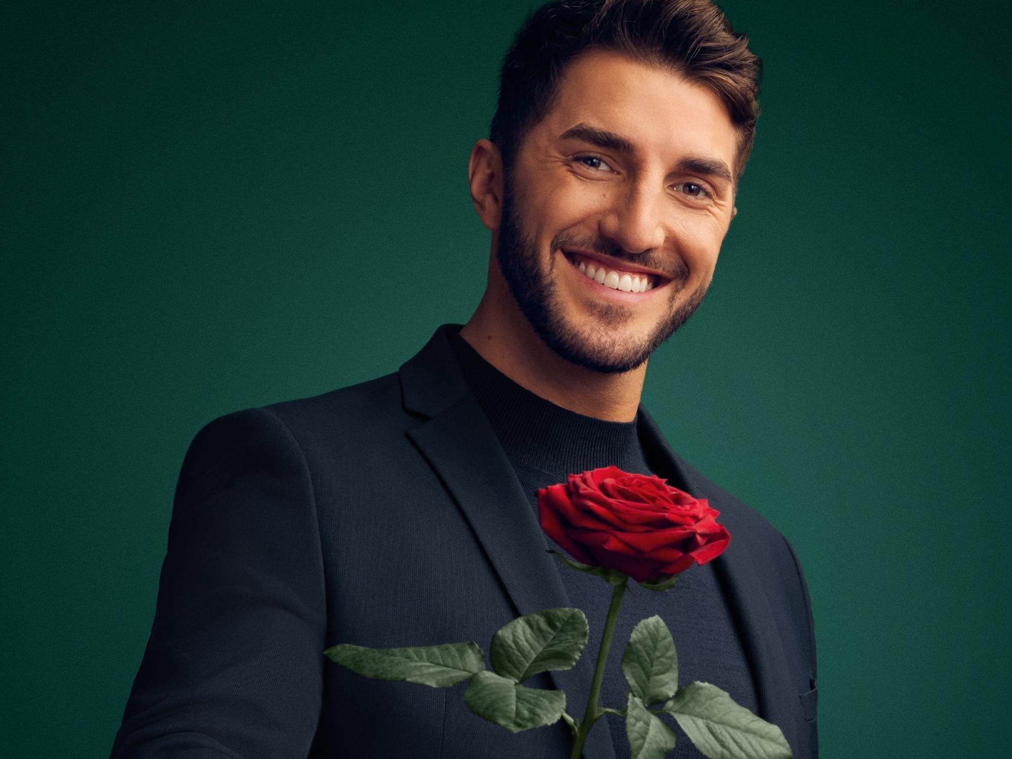 Dennis Gries lächelt in die Kamera und hält eine Rose in der Hand.