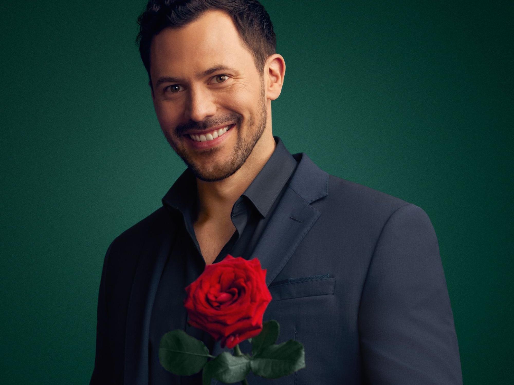 Sebastian Klaus lächelt in die Kamera und hält eine Rose in der Hand.