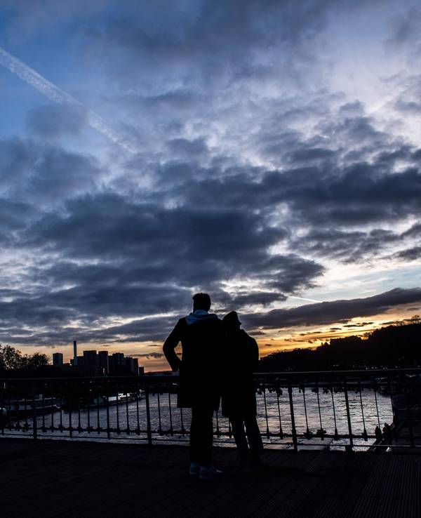 Ein Paar steht auf der Debilly-Fußgängerbrücke an der Seine und betrachtet den Sonnenuntergang hinter dem Eiffelturm.