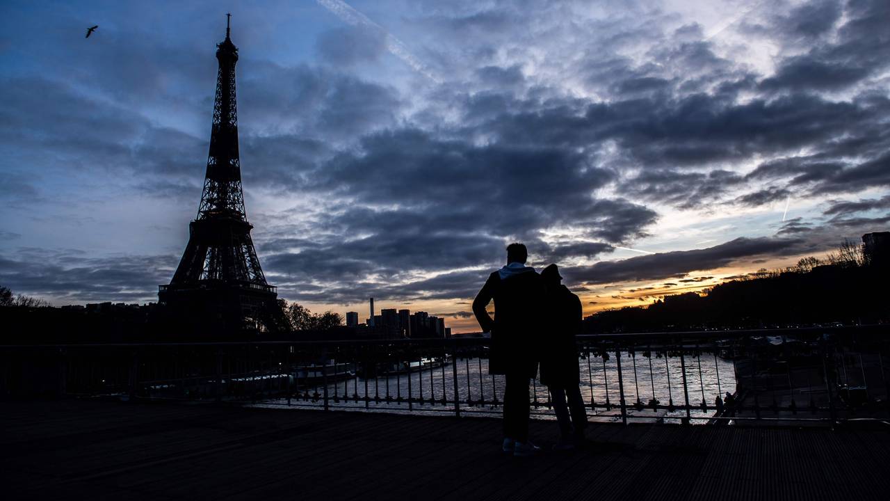 Ein Paar steht auf der Debilly-Fußgängerbrücke an der Seine und betrachtet den Sonnenuntergang hinter dem Eiffelturm.