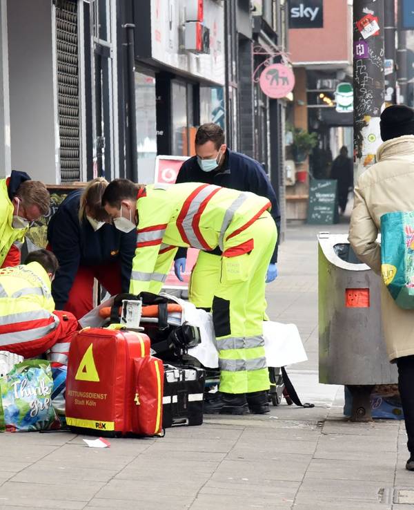 Rettungssanitäter und Notarzt kümmern sich um einen Obdachlosen an einem Straßenrand.