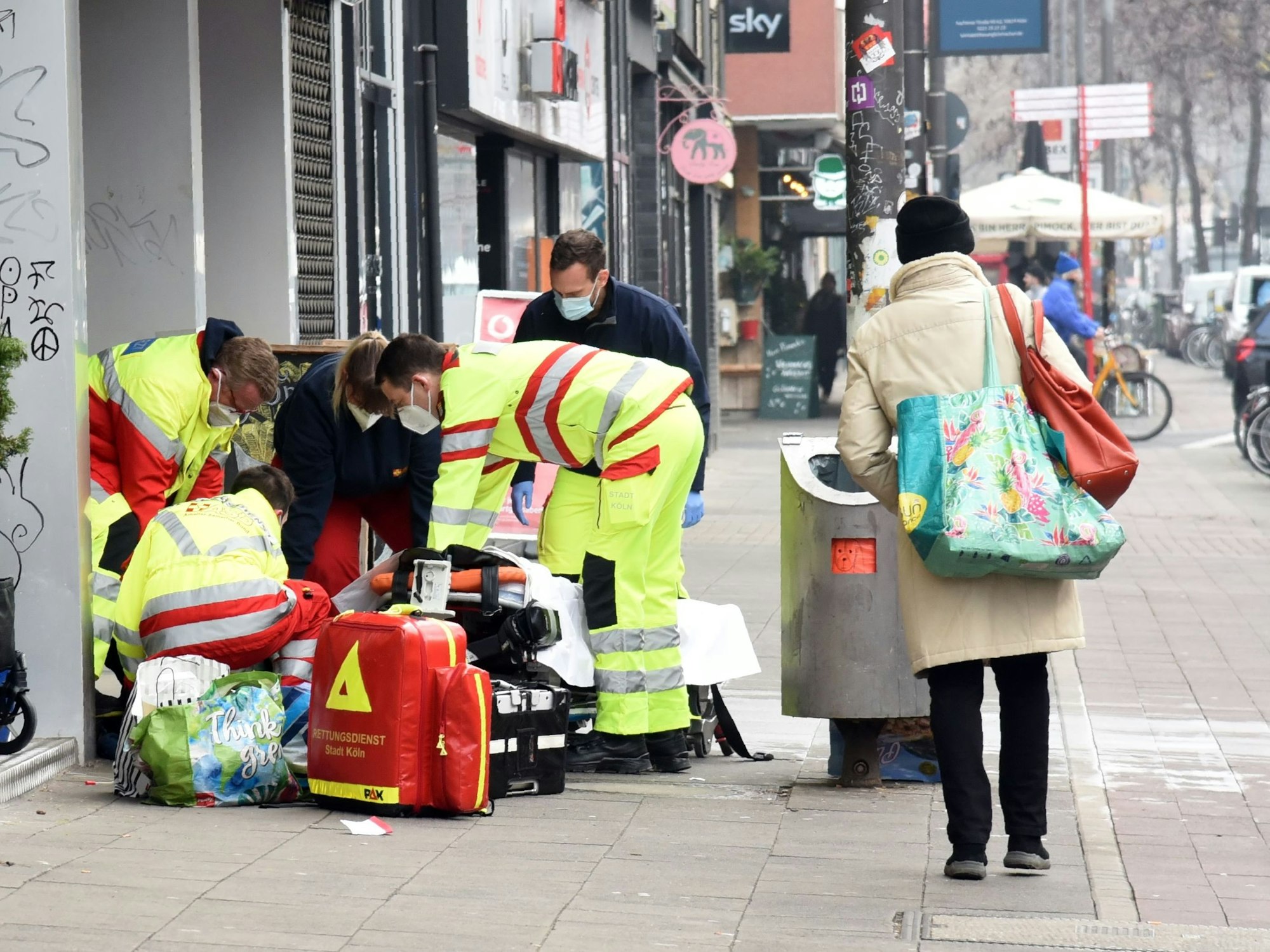 Rettungssanitäter und Notarzt kümmern sich um einen Obdachlosen an einem Straßenrand.