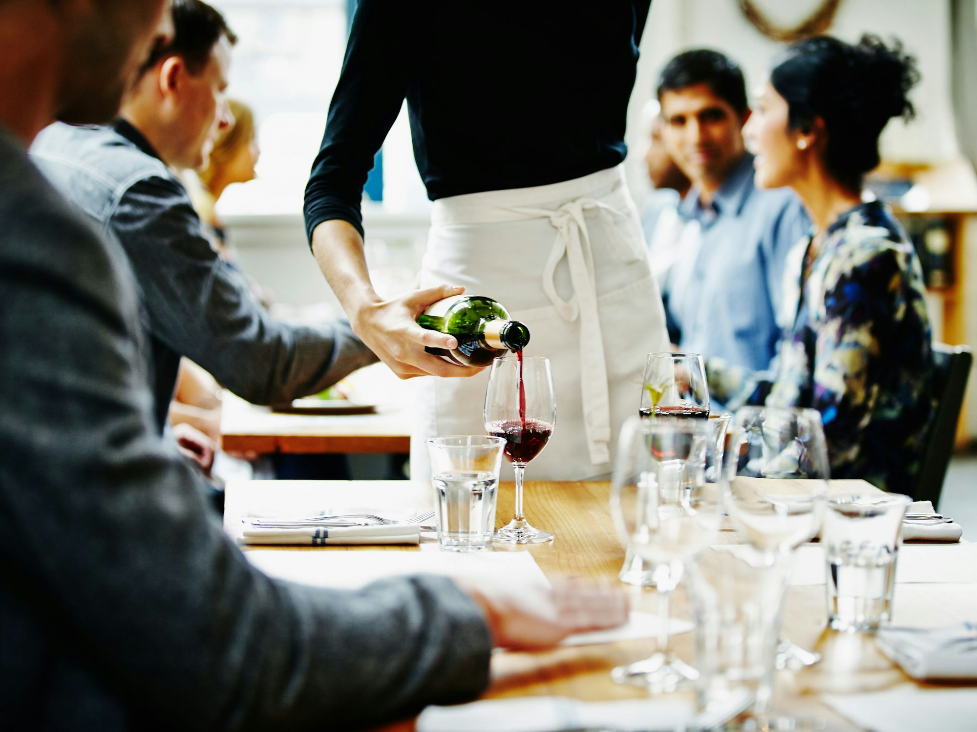Hier zu sehen: Eine Kellnerin schüttet Wein in ein Glas in einem Restaurant.