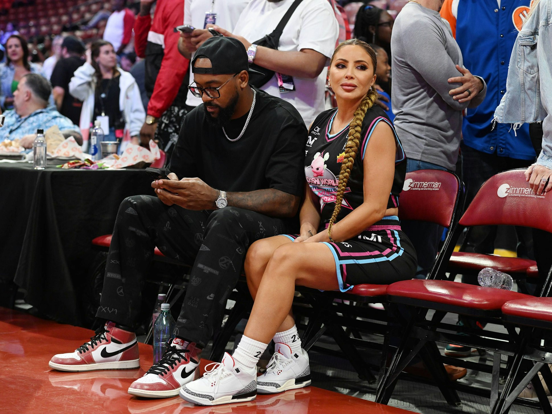 Larsa Pippen und Marcus Jordan sitzen am Rand eines Basketball-Spielfelds.