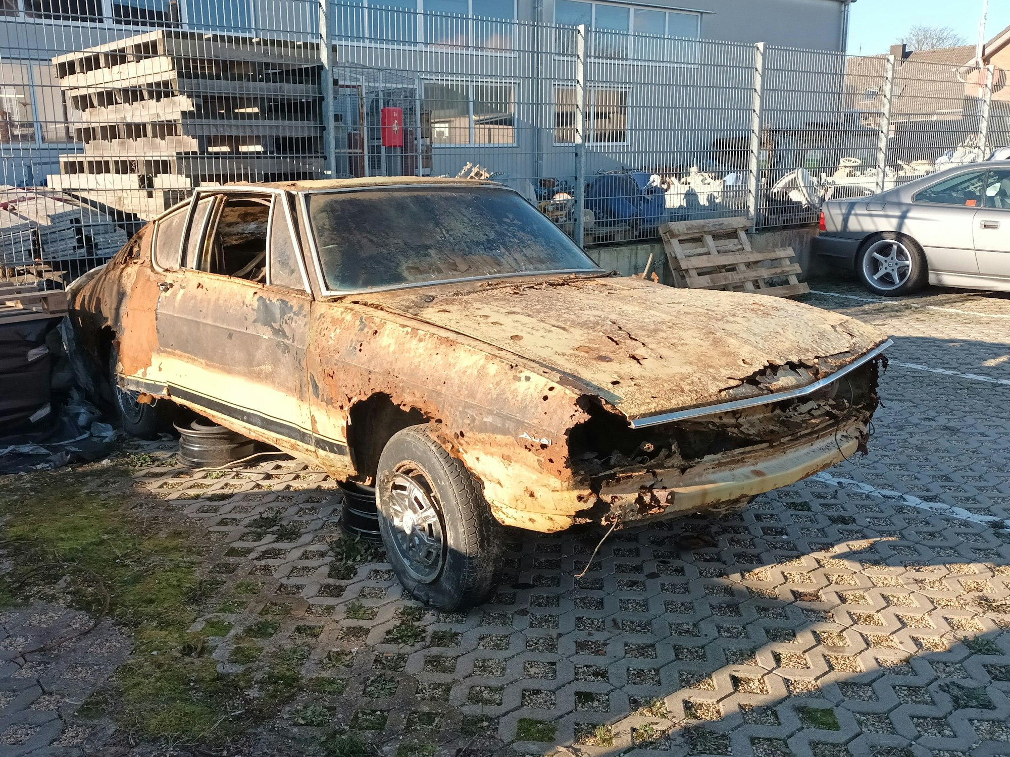 Der verrostete Audi 100 steht auf dem Hof eines Autohauses in Bergheim.