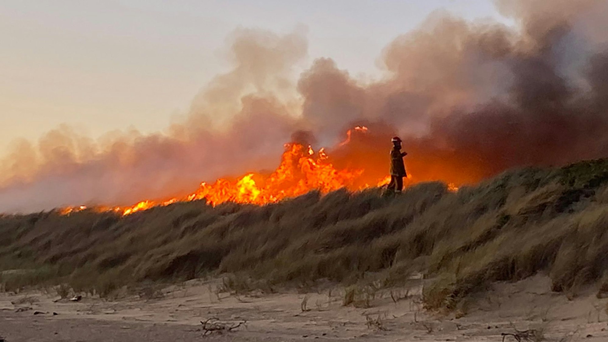 Das am Montag, 13. November 2023 (Ortszeit) aufgenommene Foto zeigt ein Feuer in Tasmanien und einen Feuerwehrmann, der vor den Flammen steht,