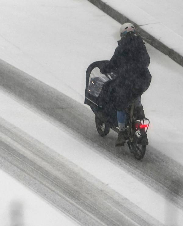 Eine Frau fährt mit einem Lastenfahrrad über eine verschneite Straße.